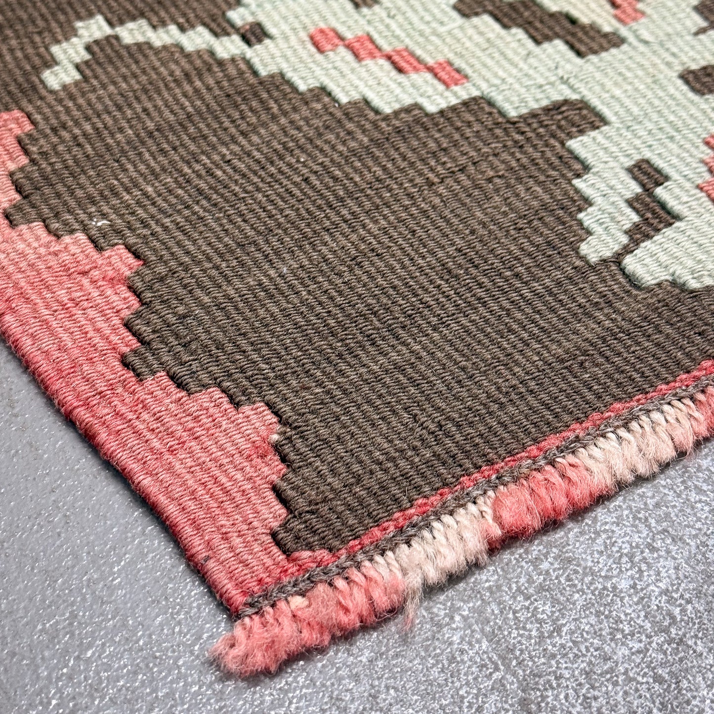 Close-up of a patterned rug with brown, pink, and beige colors on a gray surface.