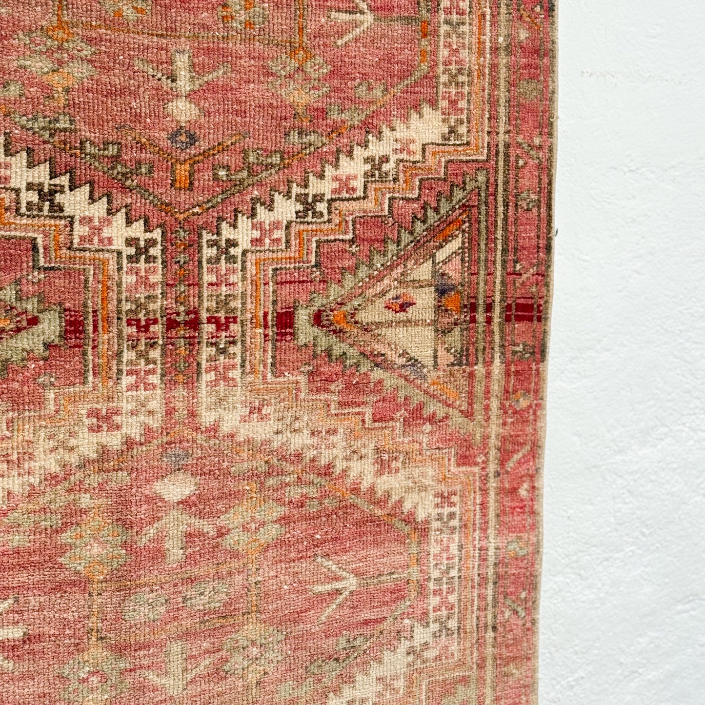 Close-up of a patterned rug with pink and beige colors on a white background
