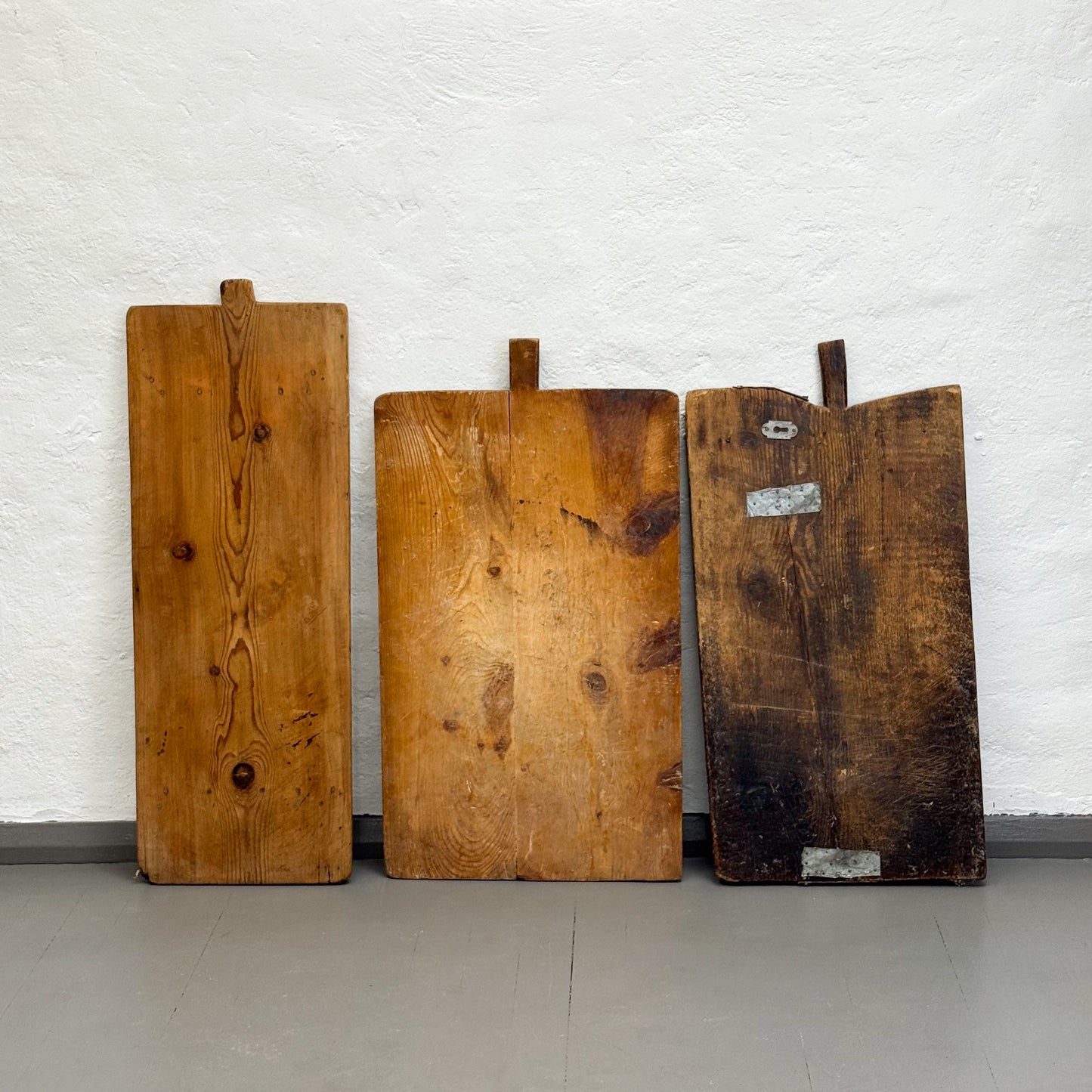 Three wooden cutting boards of varying sizes against a white brick wall.