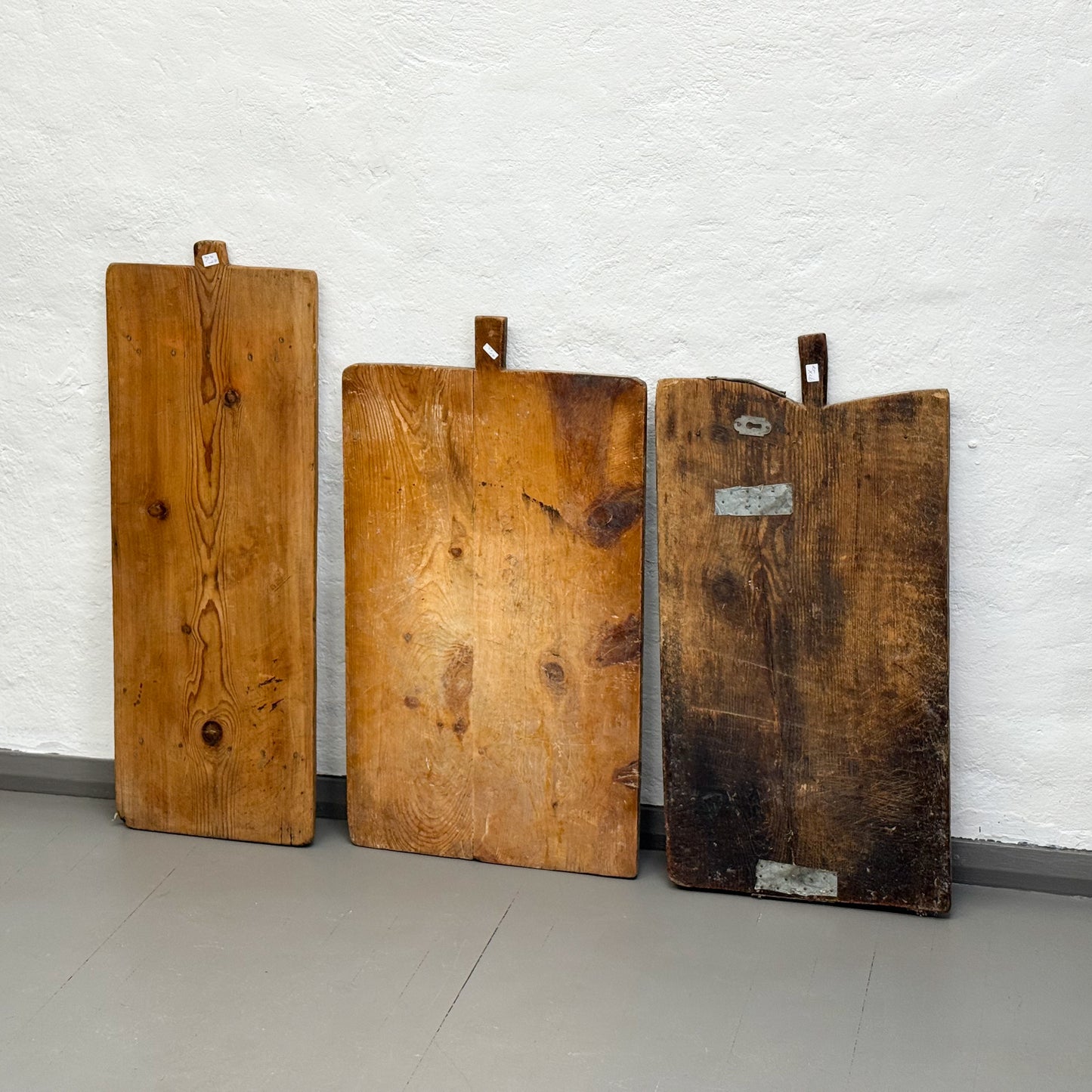 Three wooden cutting boards of varying sizes against a white brick wall.