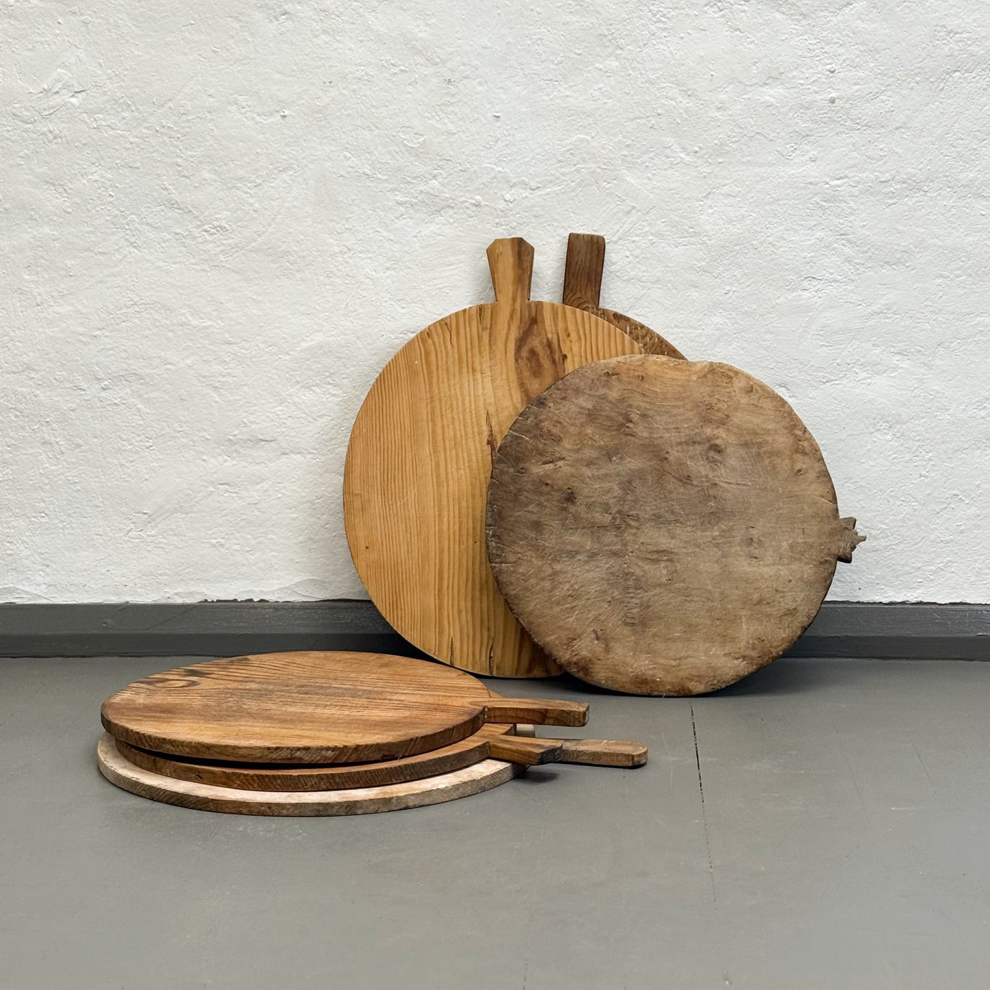 Set of wooden pizza peel tools against a textured white wall.