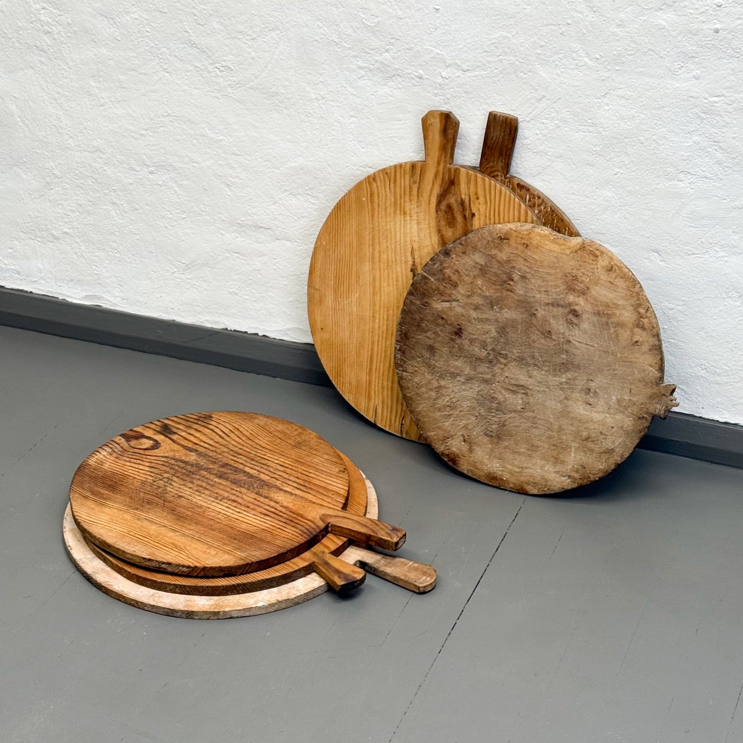 Set of wooden pizza peel tools on a gray floor against a white wall.