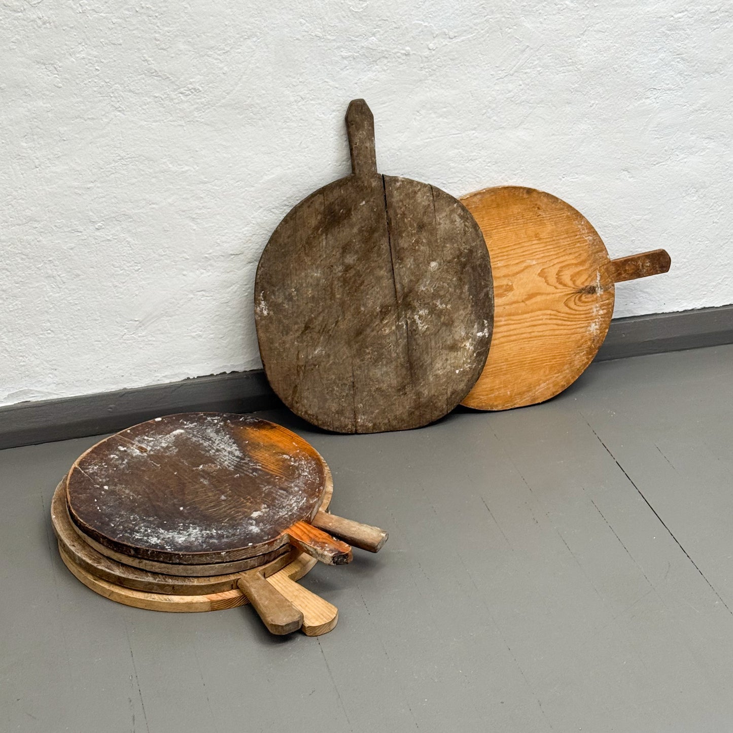 Set of wooden pizza peel tools on a gray floor against a white wall.