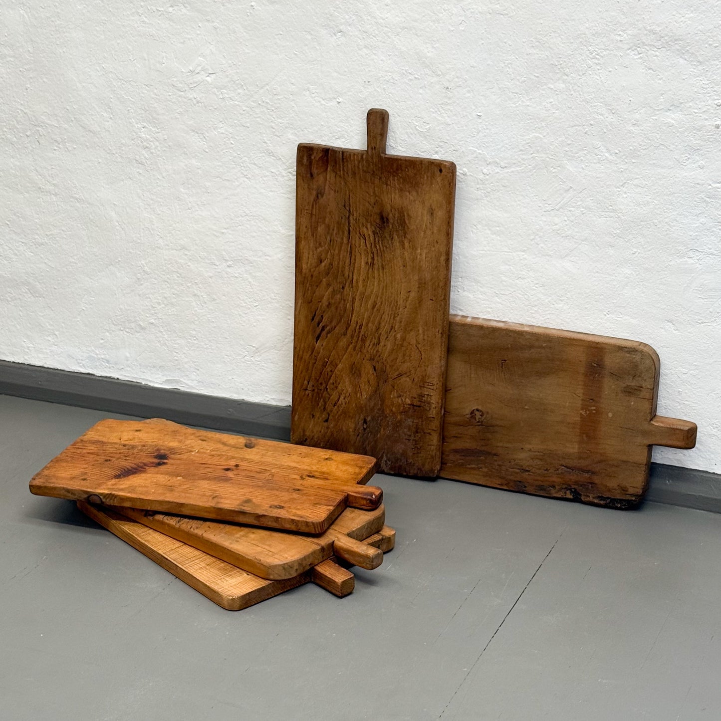 Set of wooden cutting boards on a gray floor against a white wall