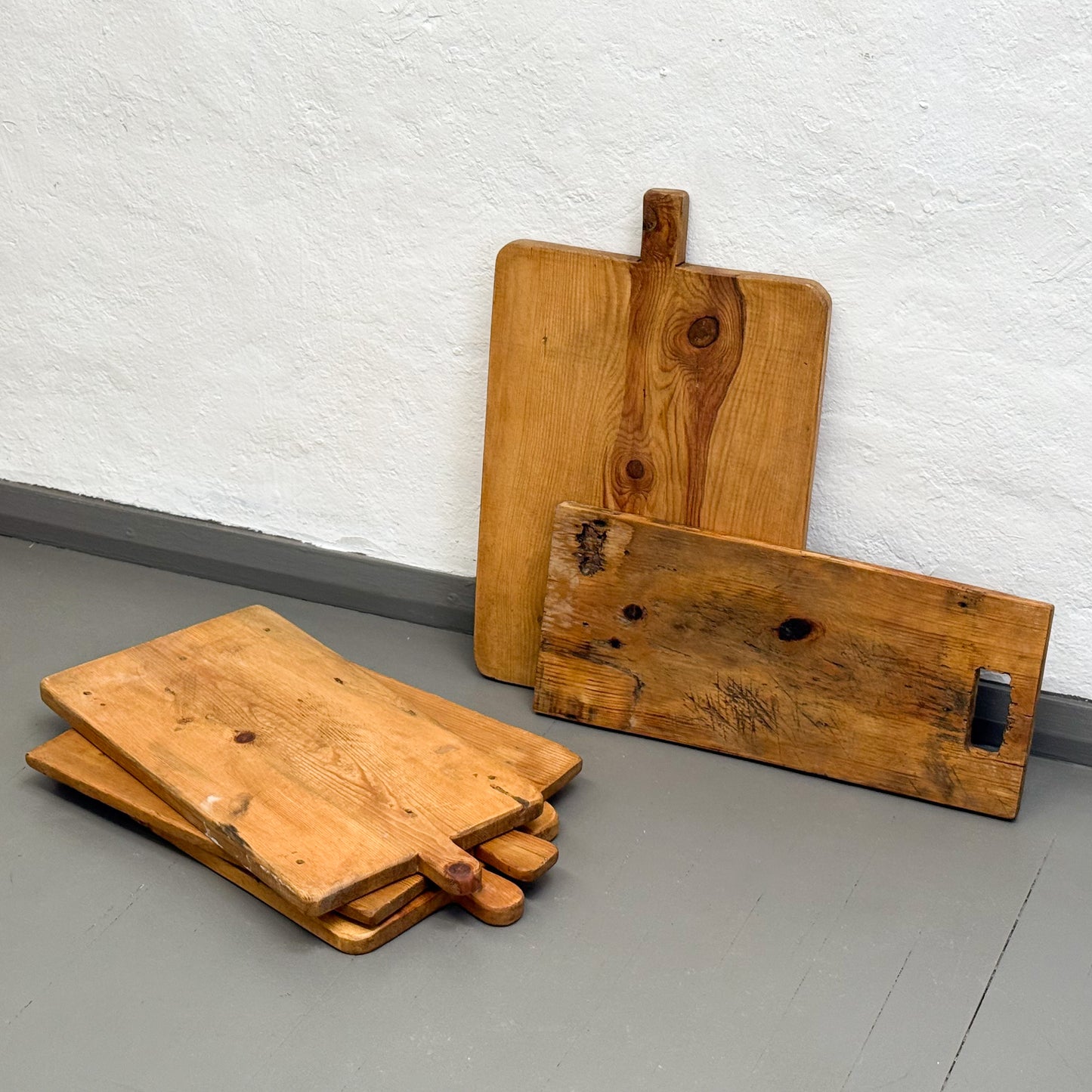 Three wooden cutting boards of different sizes on a gray floor against a white wall.