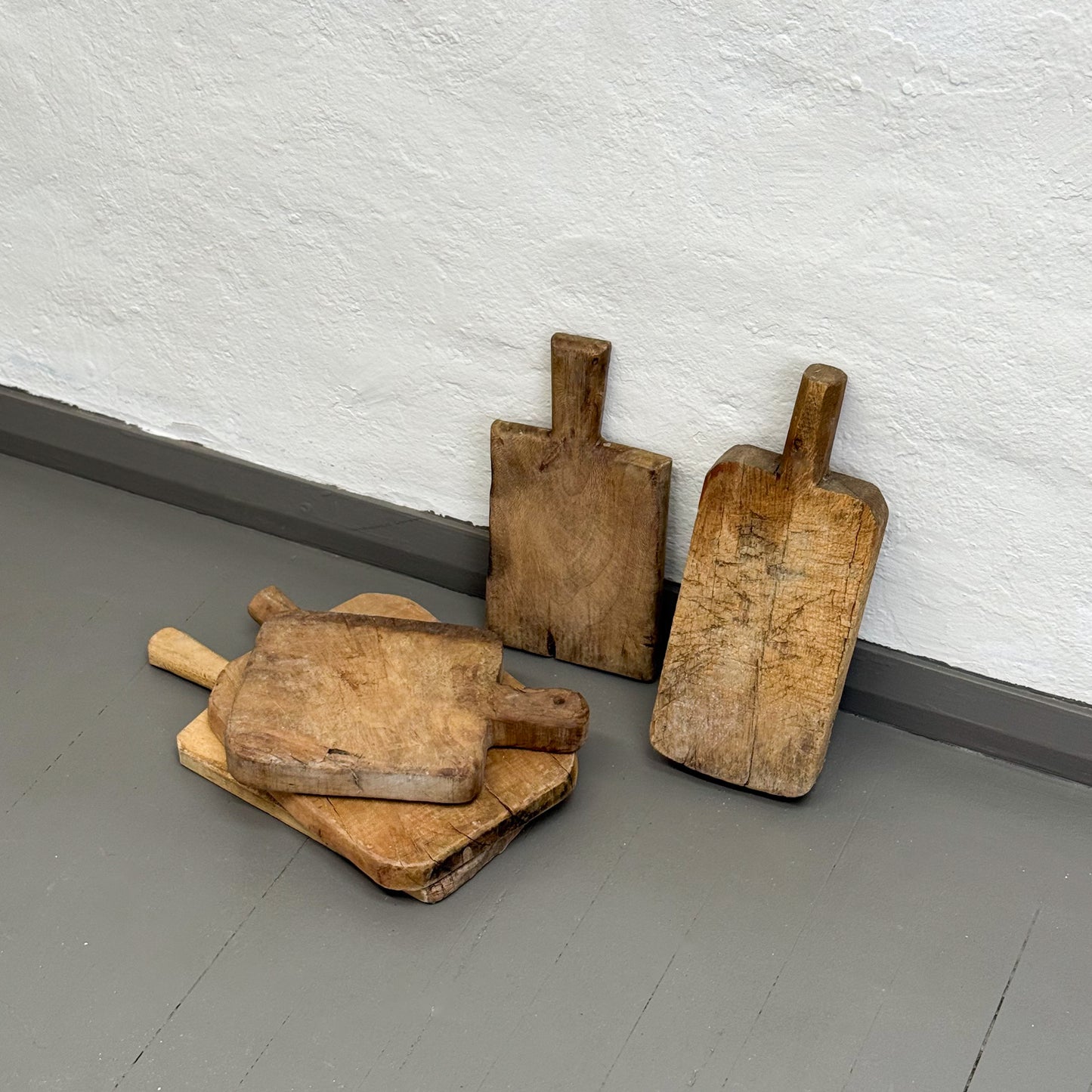 Set of wooden cutting boards on a gray floor against a white wall.