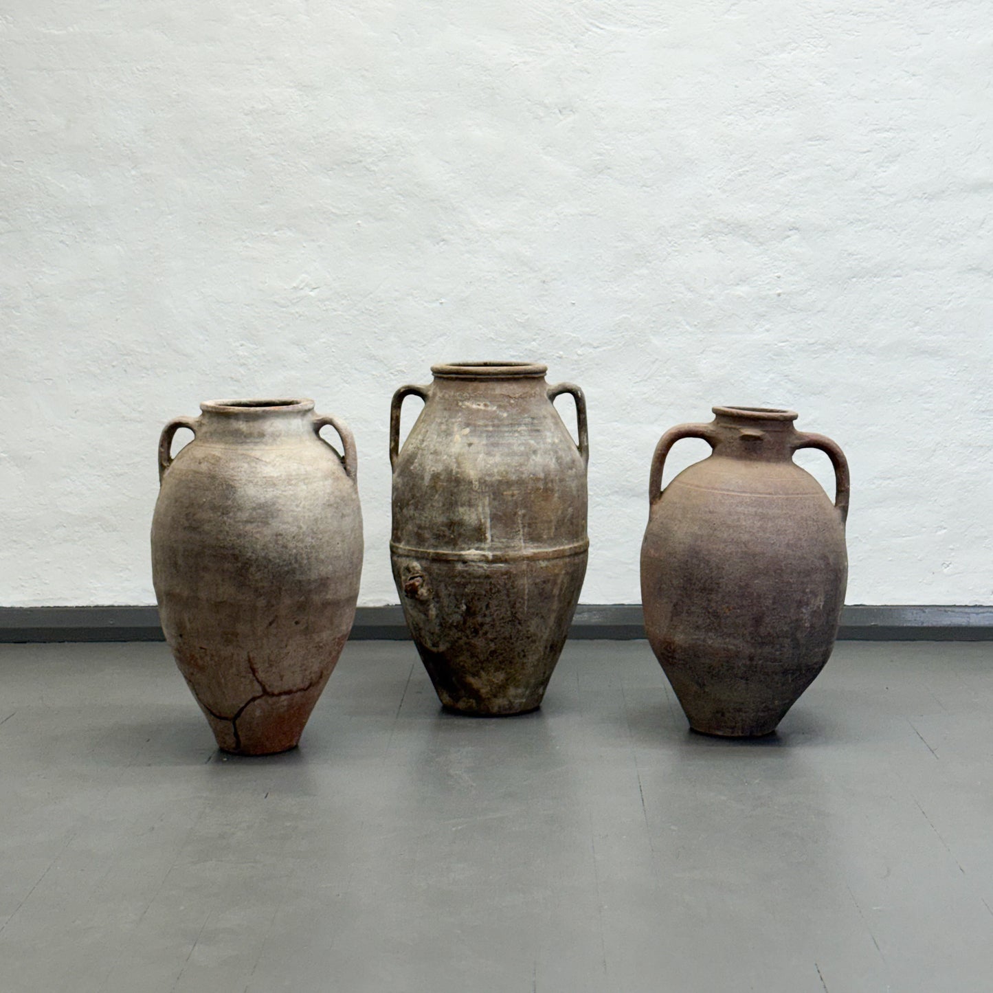 Three ancient-style clay pots on a gray floor with a white textured wall background