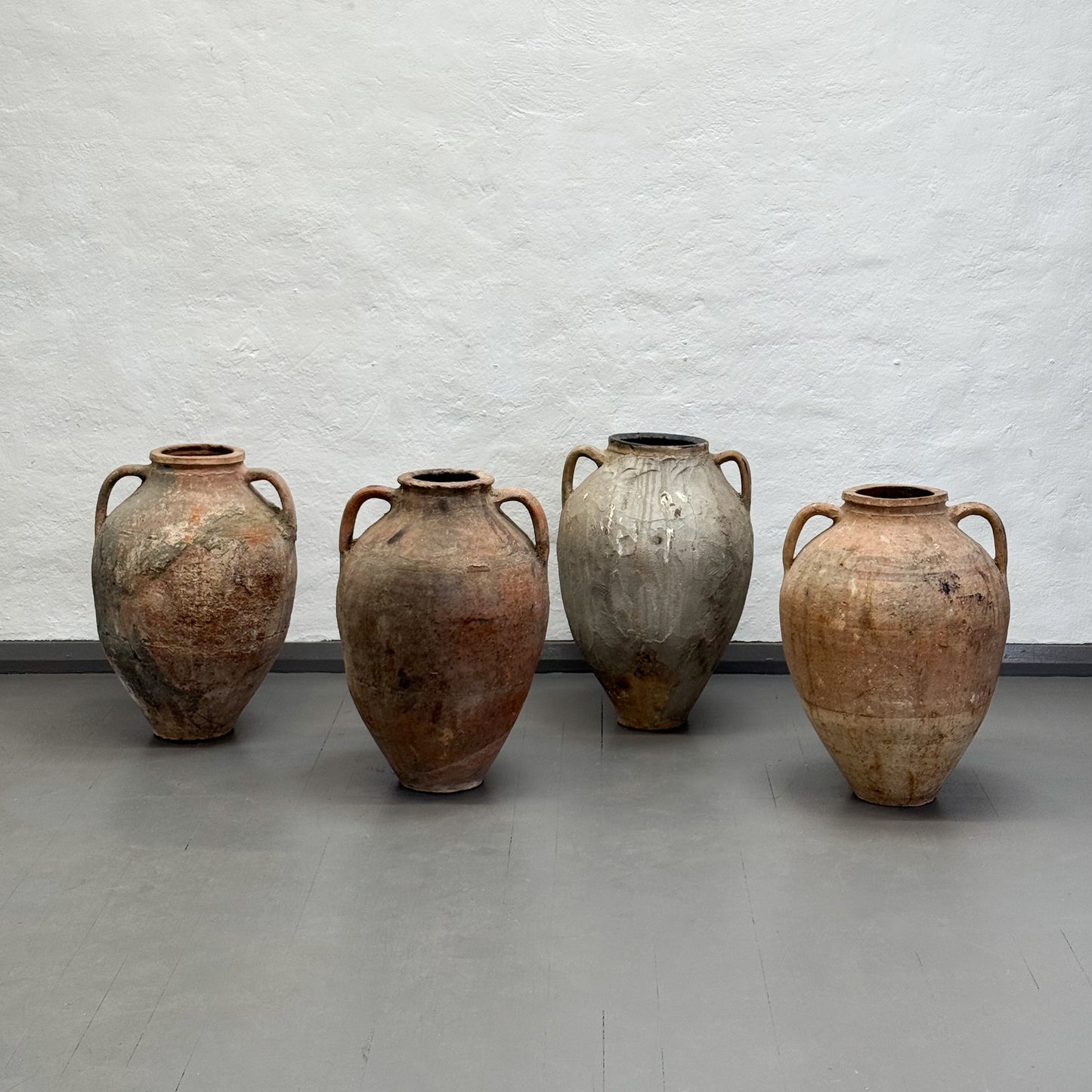Four rustic clay pots of varying sizes against a textured white wall.