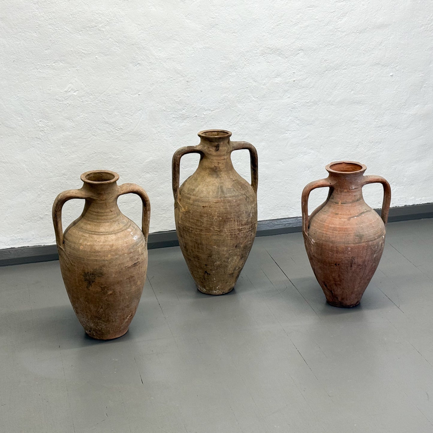 Three terracotta vases of different sizes against a white textured wall.