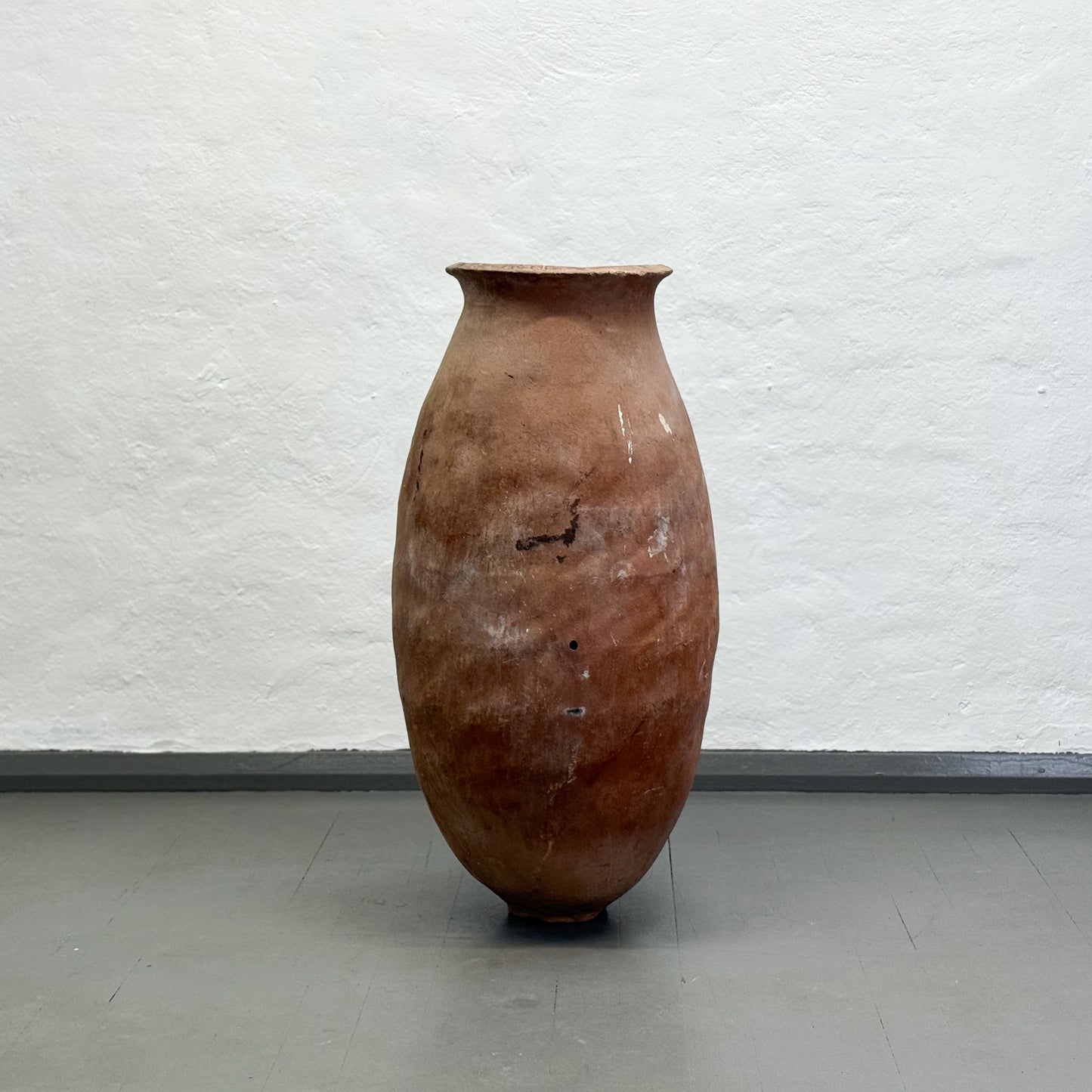 Large brown ceramic vase on a gray floor with a white textured wall background