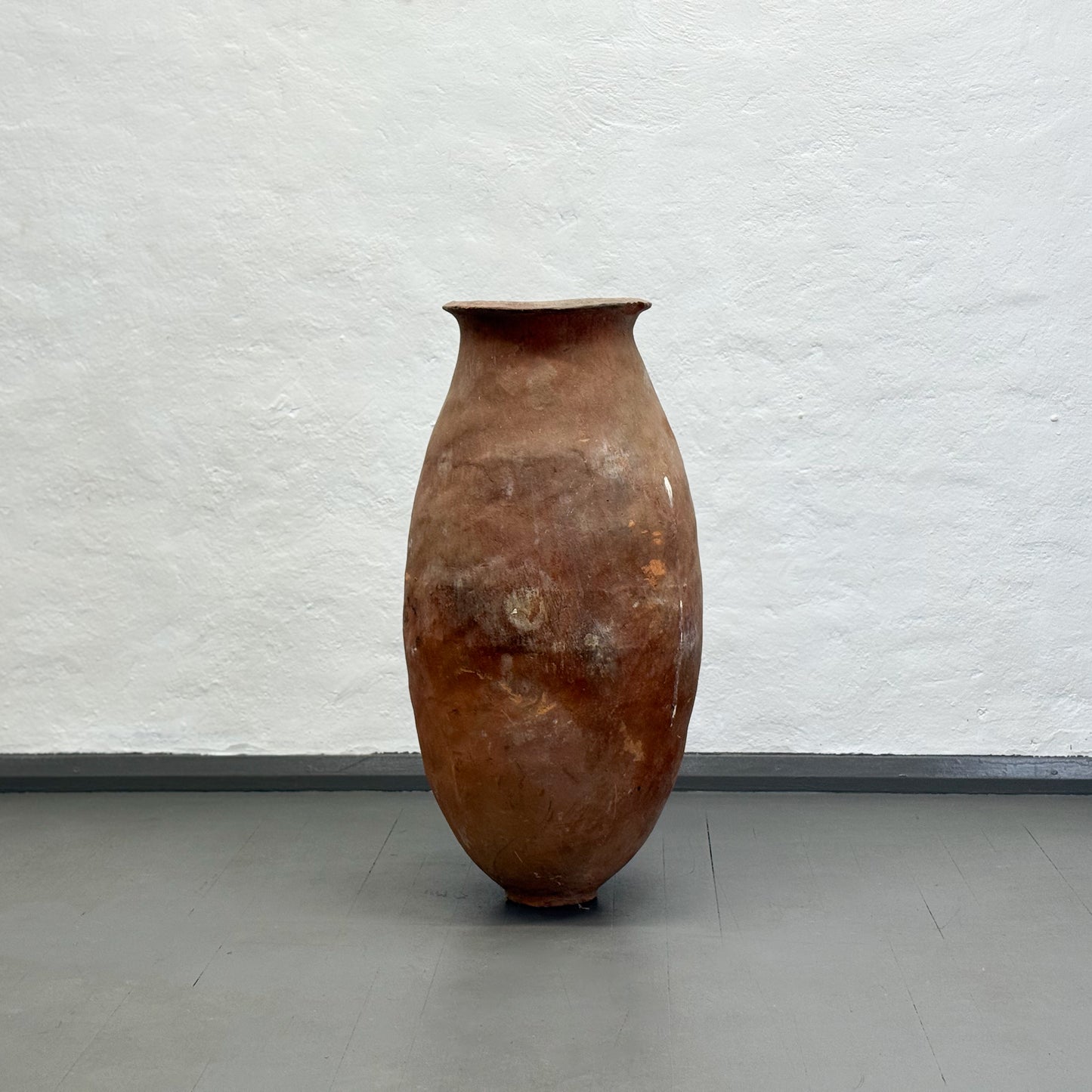 Brown ceramic vase on a gray floor with a white textured wall background