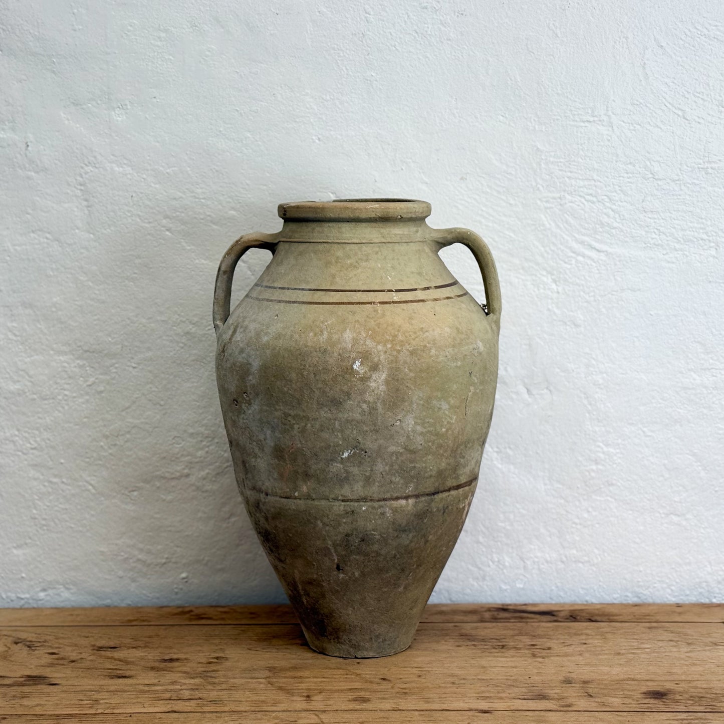 Vintage-style terracotta vase with handles on a wooden surface against a white wall