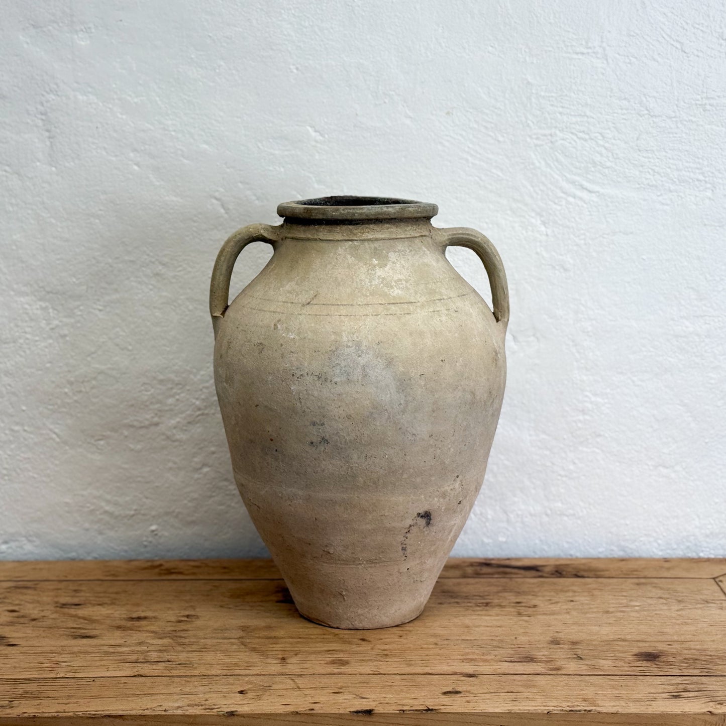 Large ceramic vase with handles on a wooden surface against a white wall
