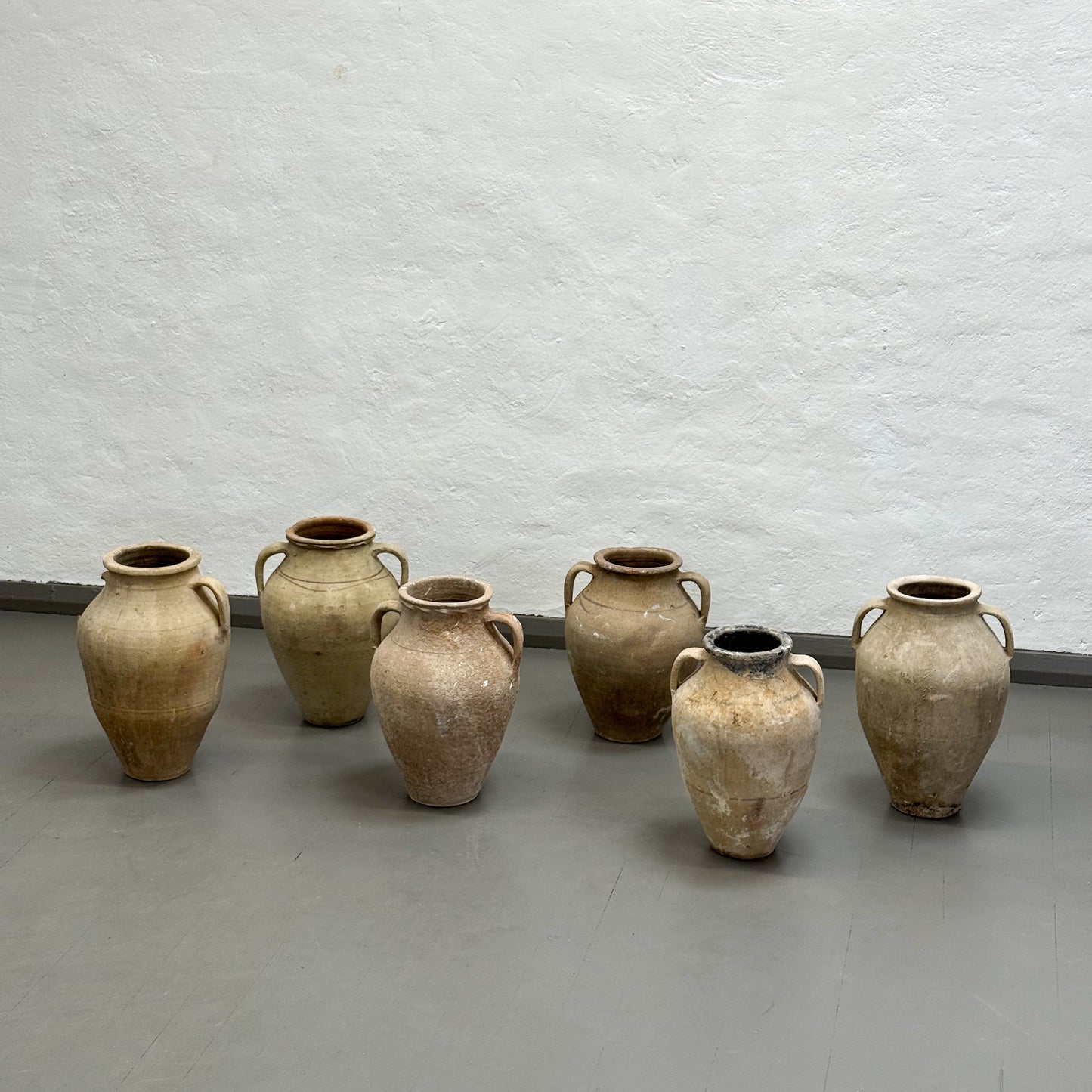 Set of six terracotta pots on a gray floor against a white textured wall.