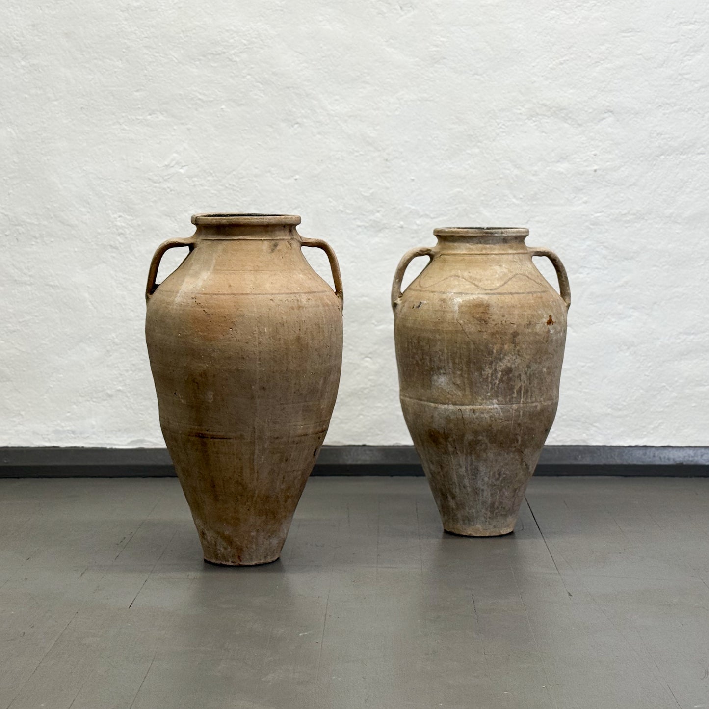 Two large brown ceramic vases against a white textured wall.