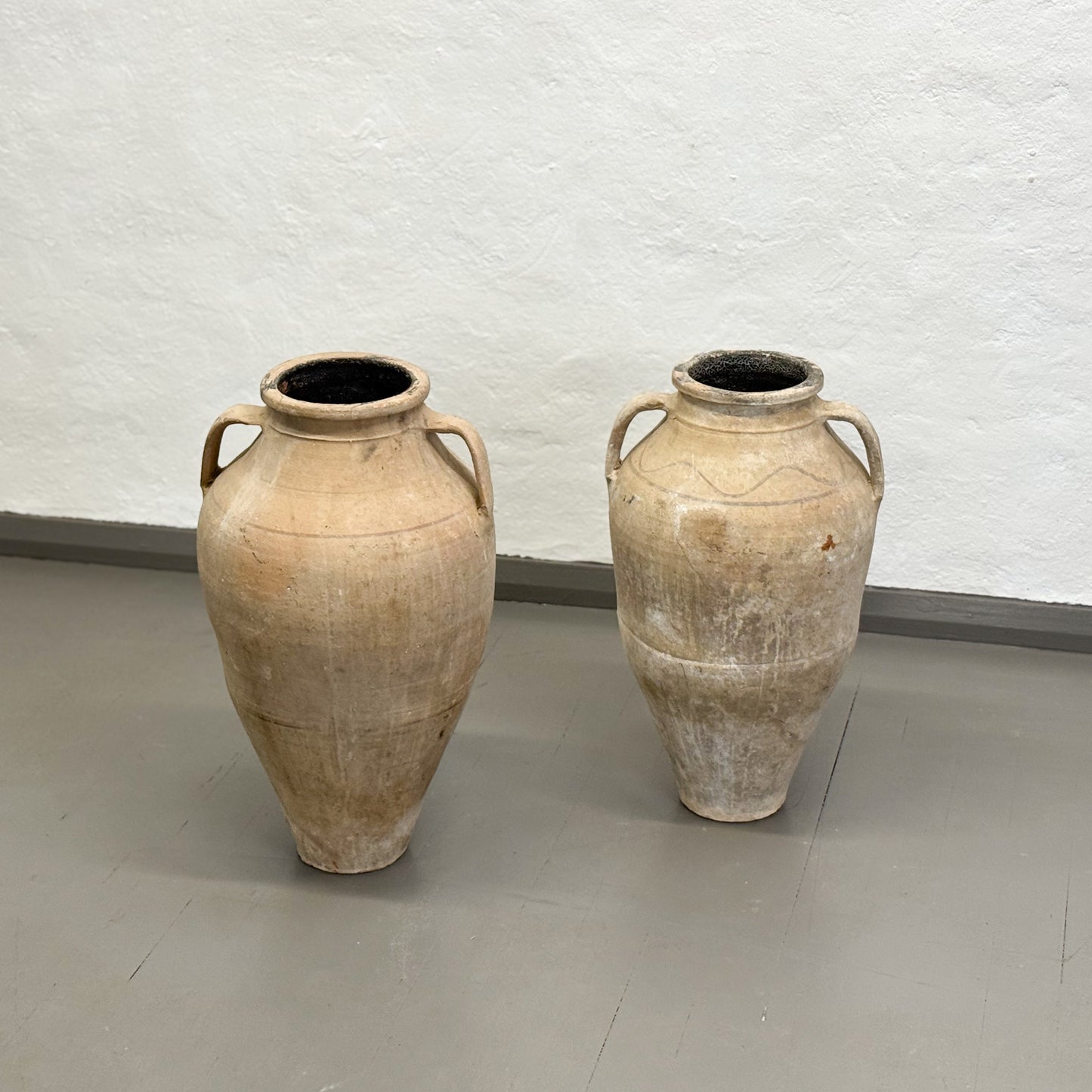 Two ancient-style clay pots on a plain floor with a light gray wall background