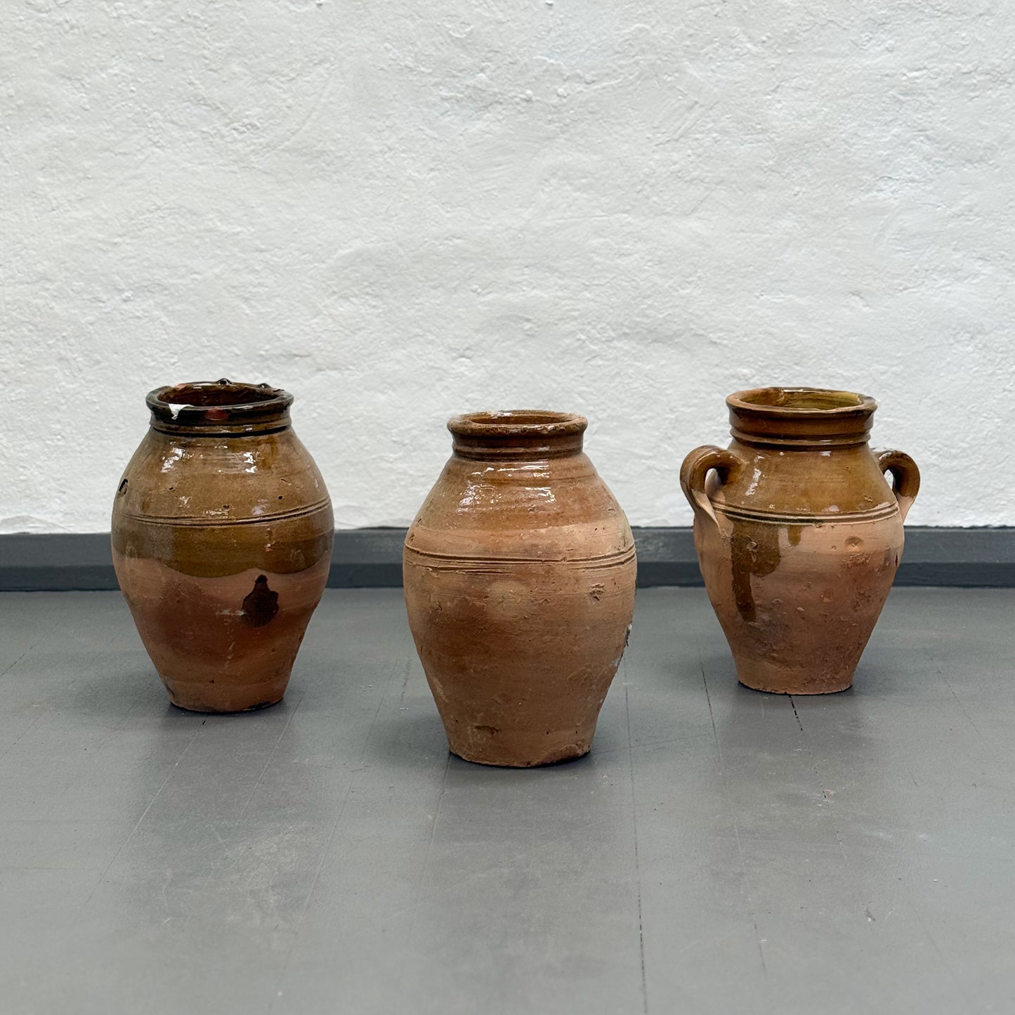 Three brown ceramic pots on a gray floor with a white textured wall background
