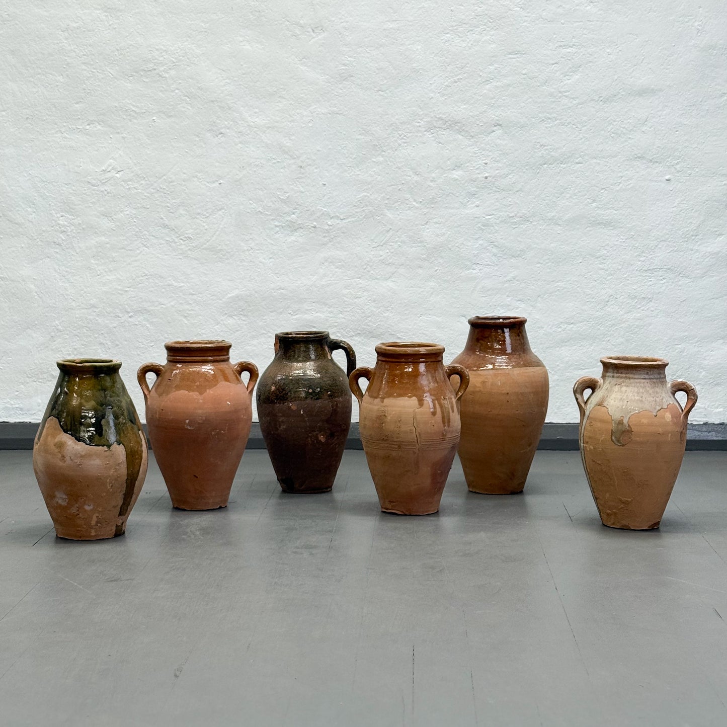 Set of six terracotta vases against a textured white wall.