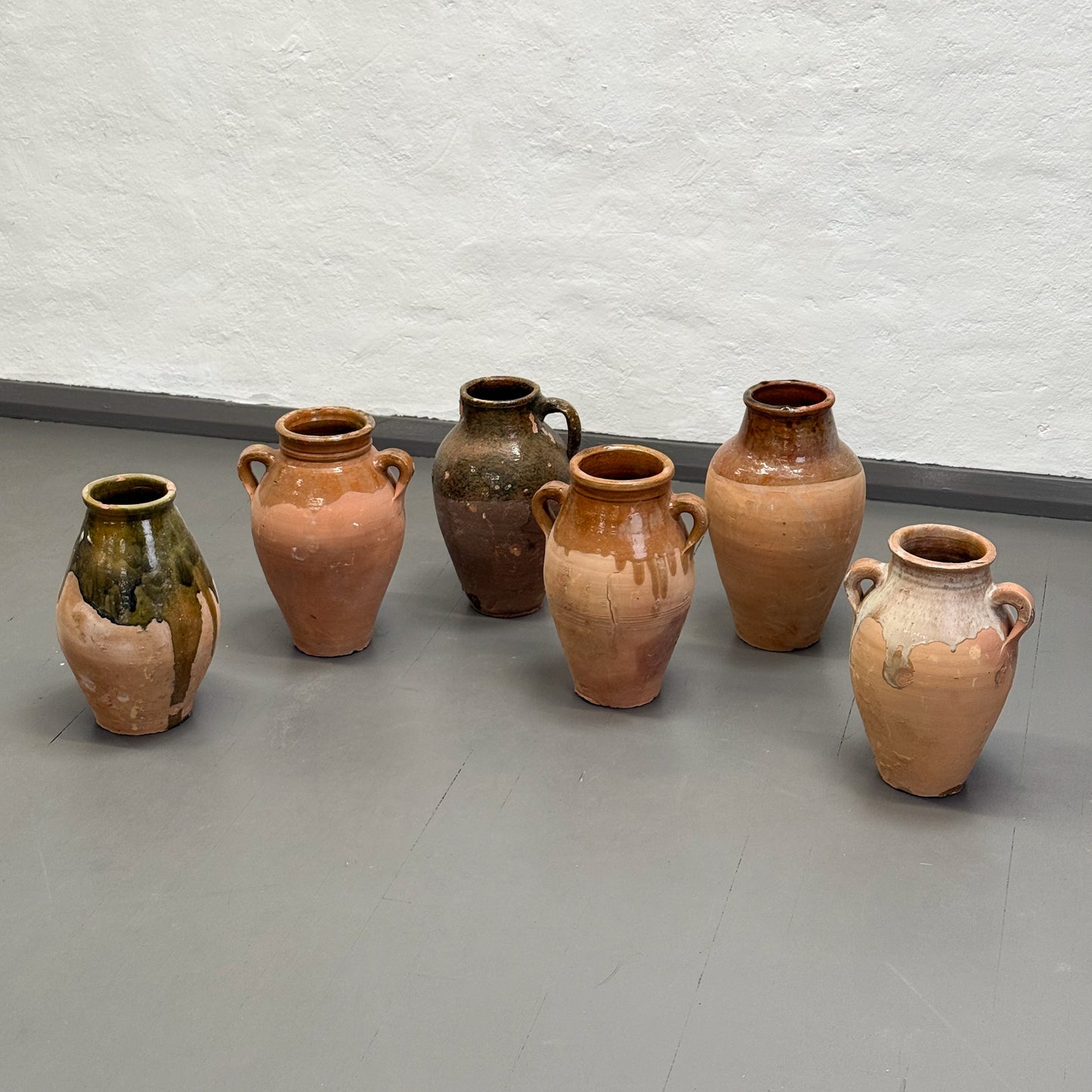 Set of six ceramic vases on a gray floor with a white wall background