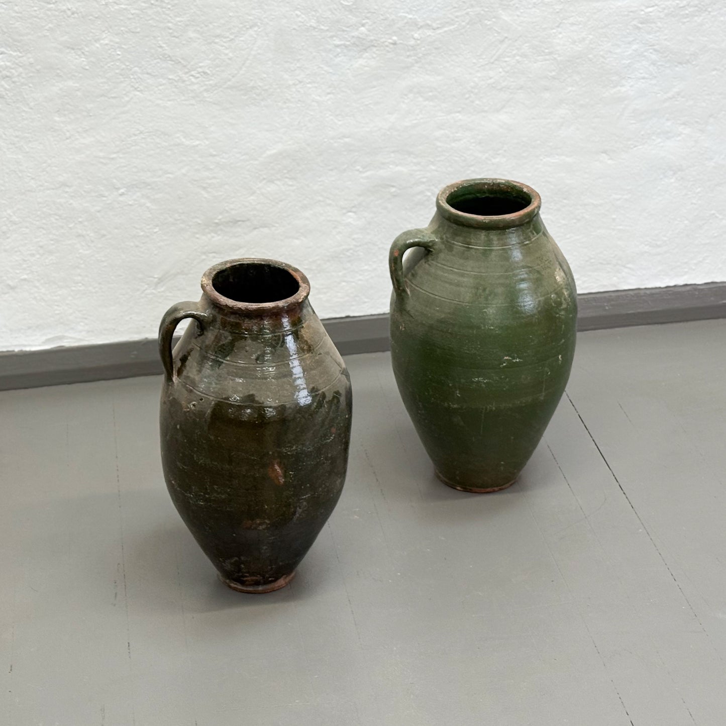 Two ceramic vases on a plain floor with a textured wall background