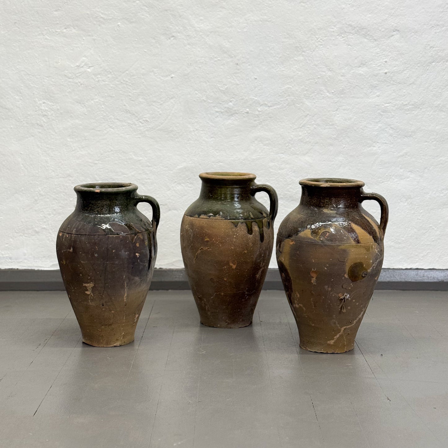 Three large brown ceramic jars against a textured white wall.