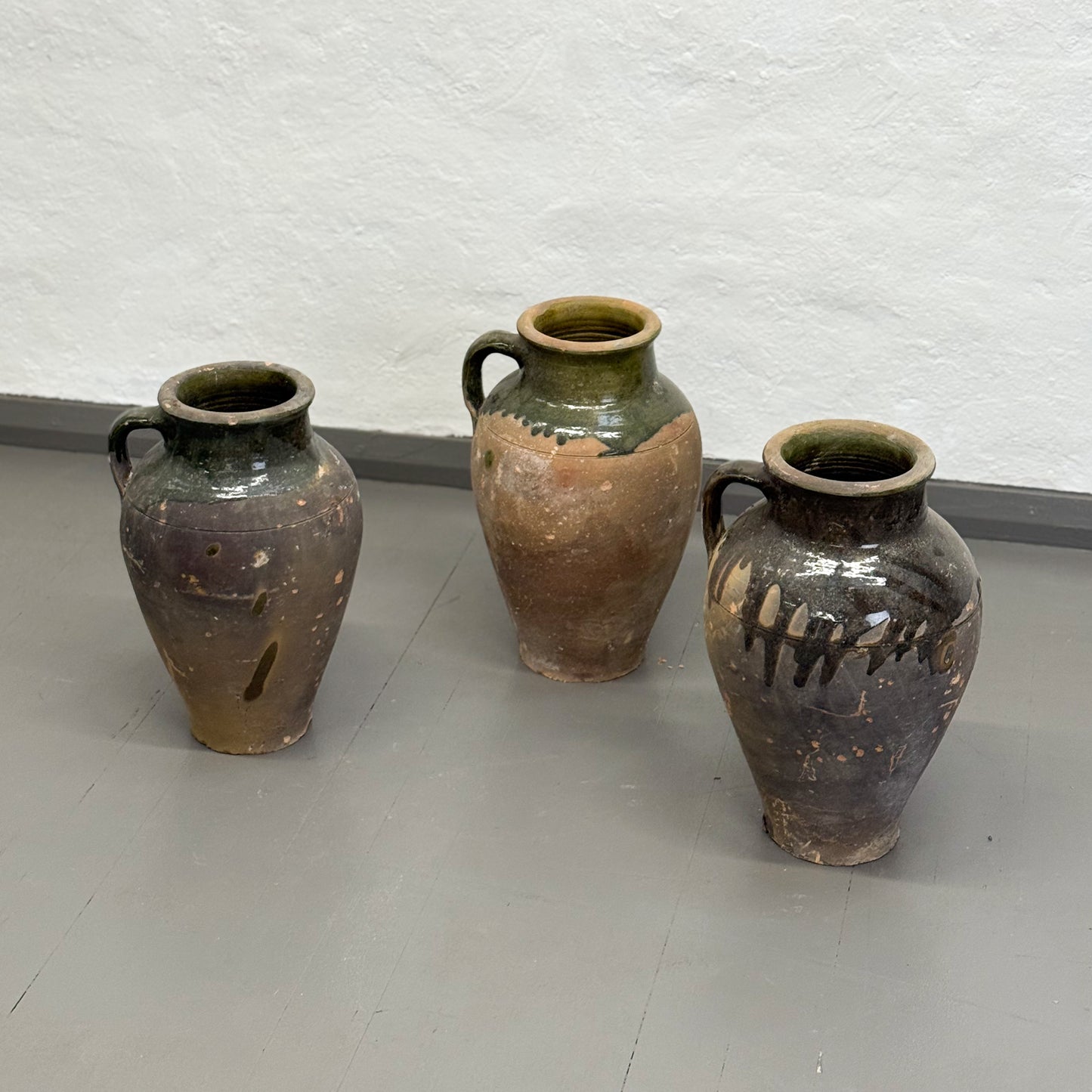 Three ceramic jars with brown and green glaze on a plain surface.