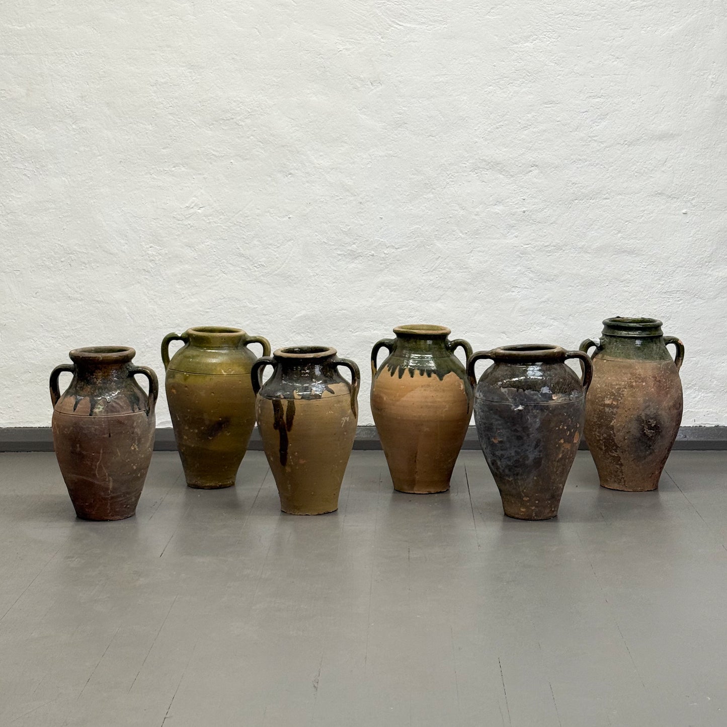 Set of seven rustic ceramic vases against a textured white wall.