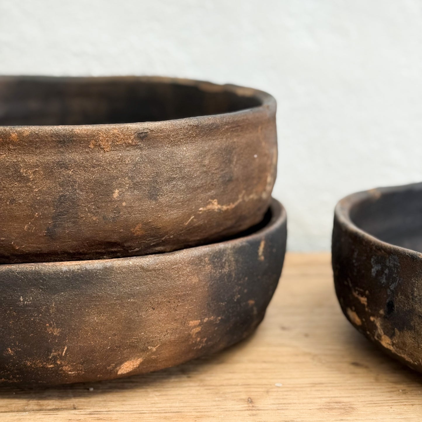 Three rustic wooden bowls on a wooden surface with a light gray background