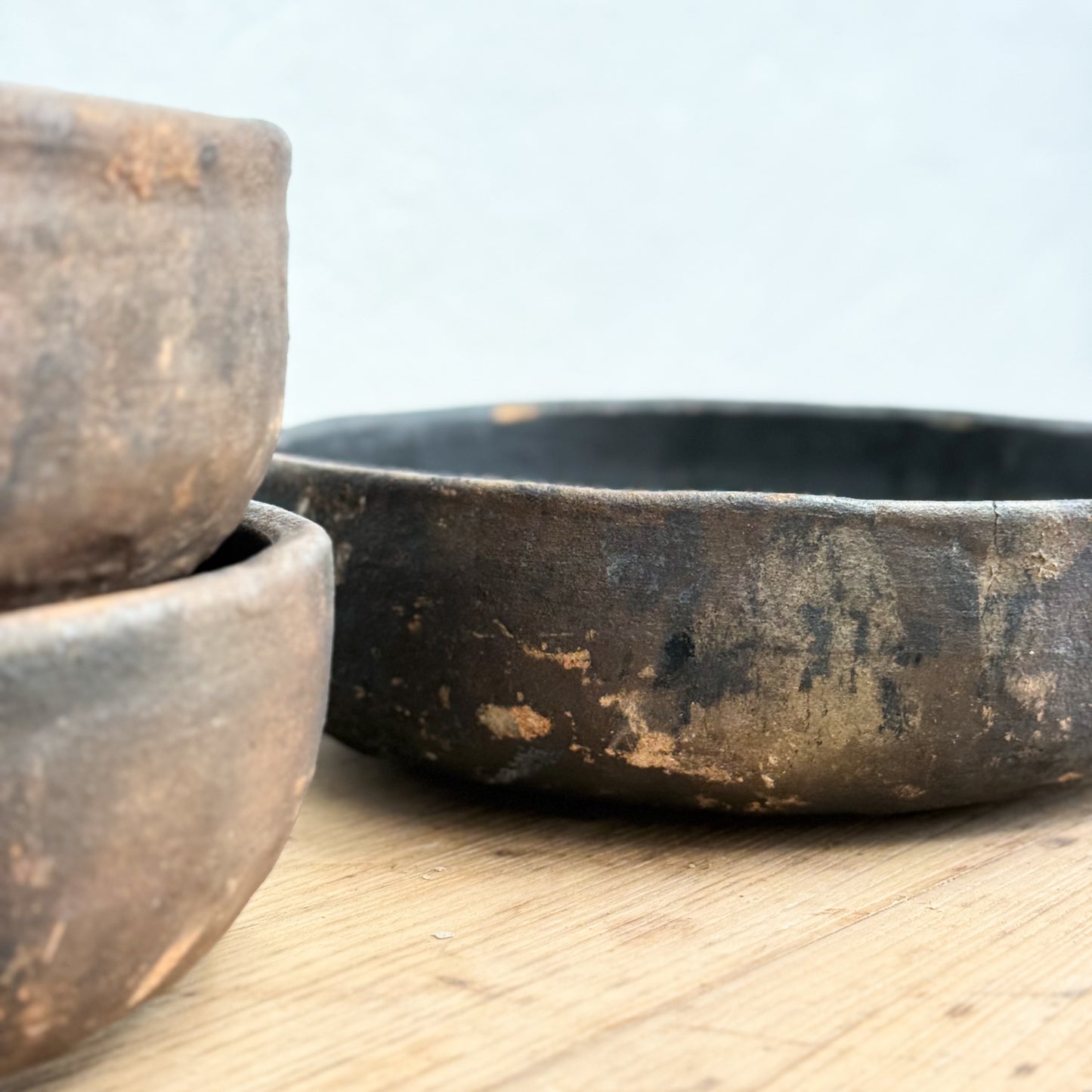 Three rustic metal bowls on a wooden surface with a light blue background