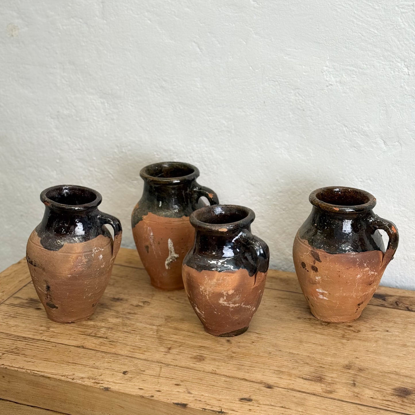 Four terracotta vases with black glaze on a wooden surface against a white wall.