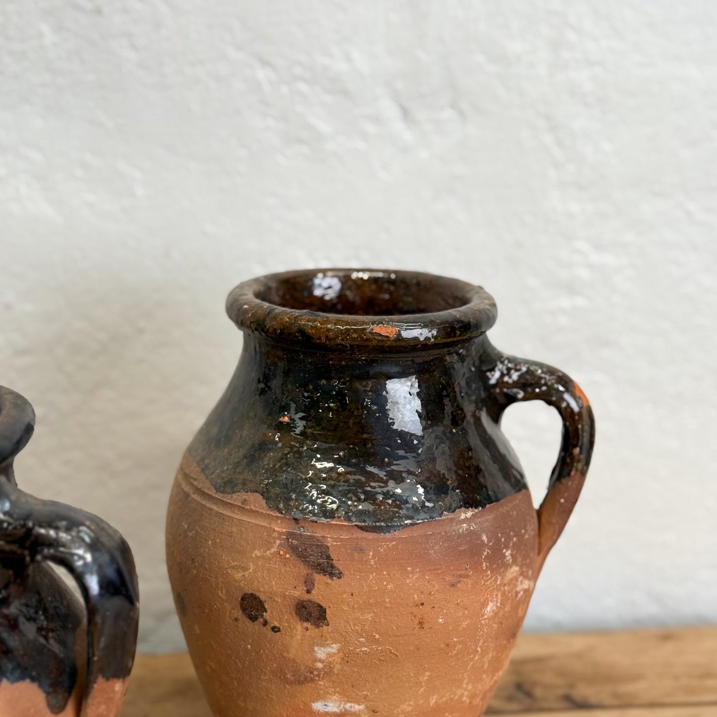 Brown ceramic jar with black glaze on a wooden surface against a white wall