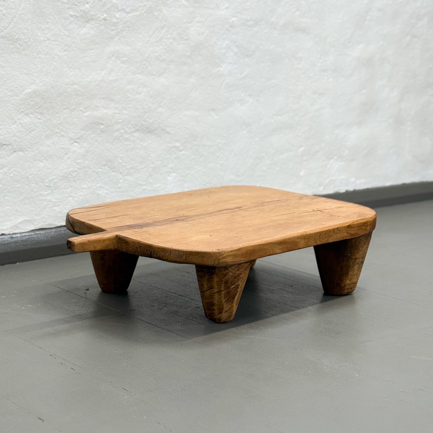 Wooden footstool on a gray floor with a light gray textured wall background