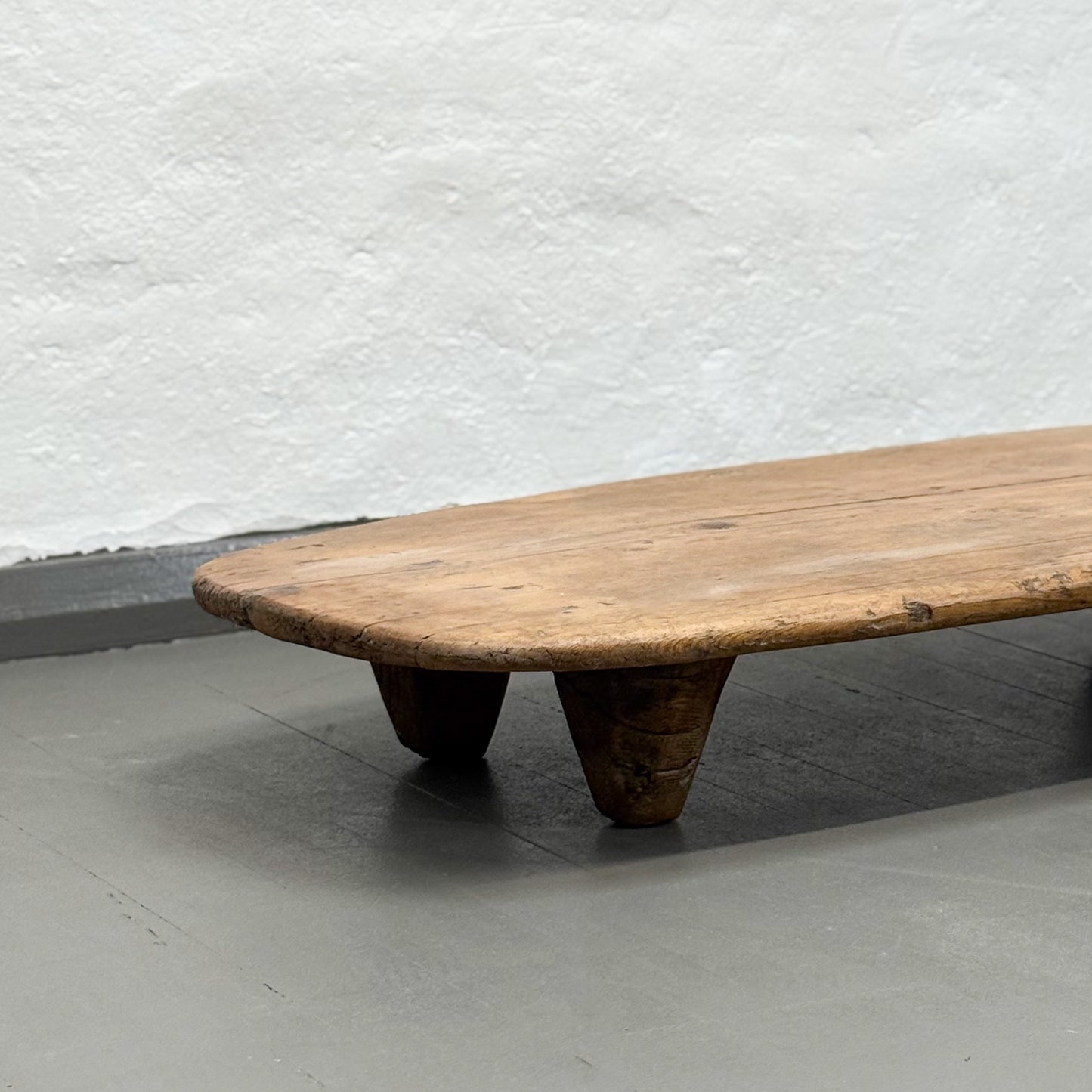 Wooden bench with unique legs against a textured white wall.