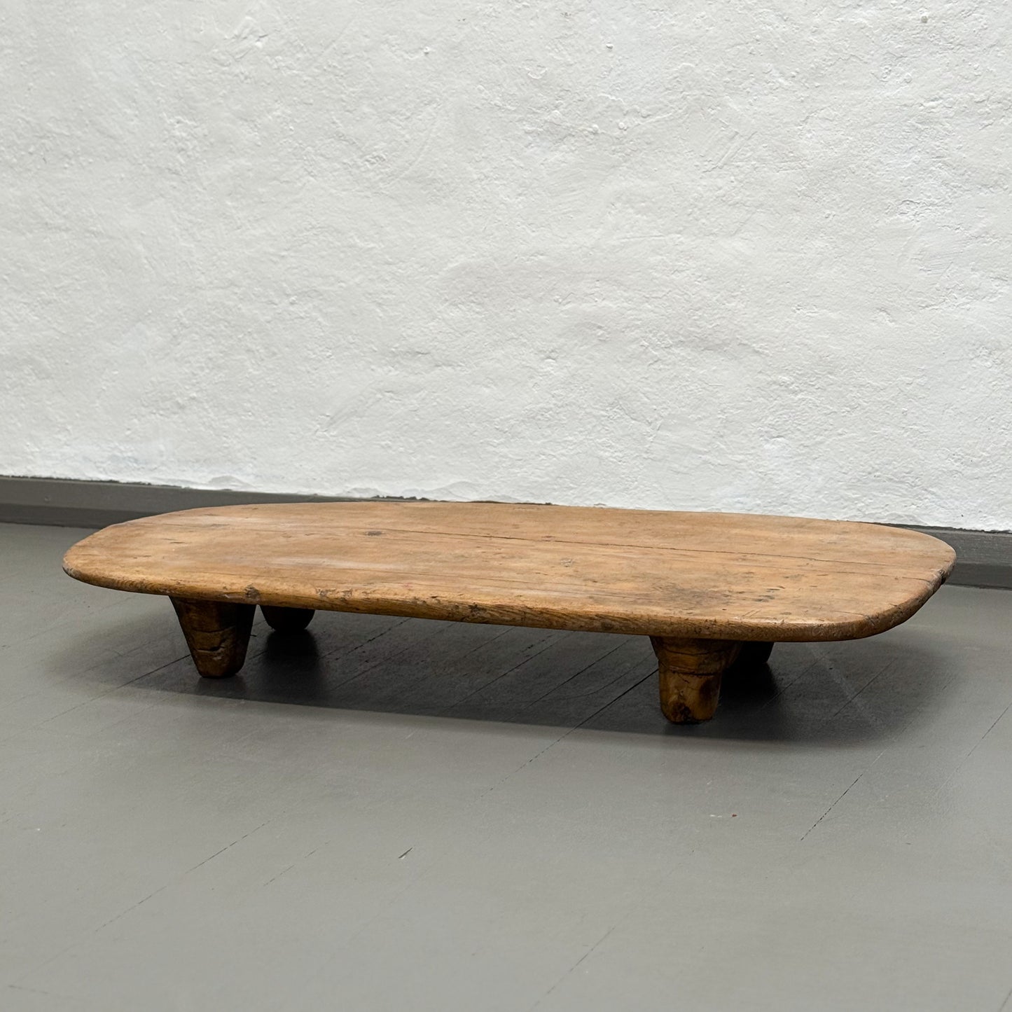 Wooden coffee table on a gray floor with a textured white wall background