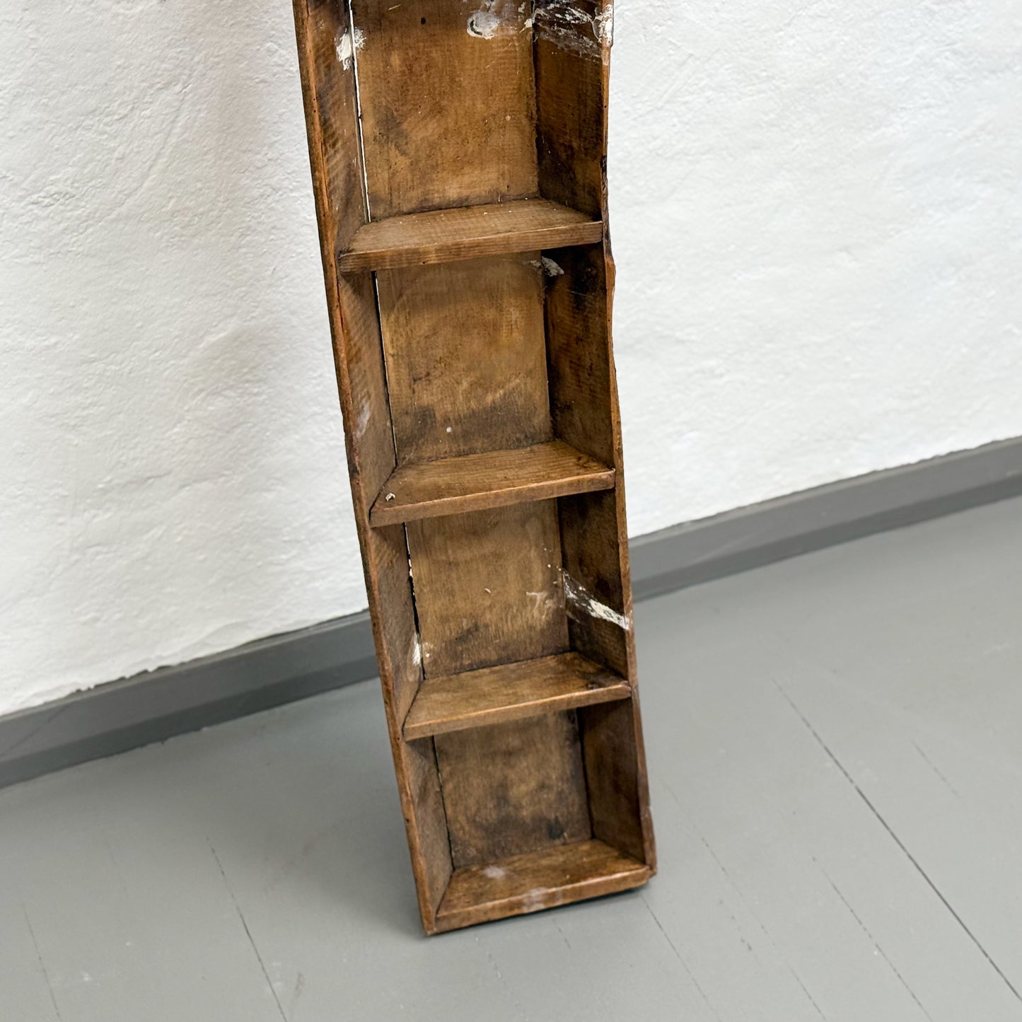 Wooden bookshelf with four shelves against a white wall.