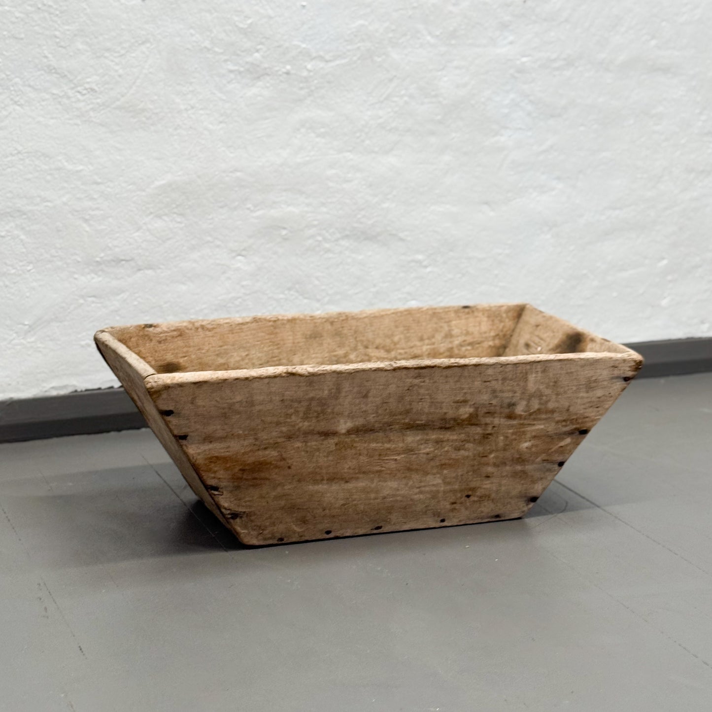 Wooden trough on a gray floor with a textured white wall background